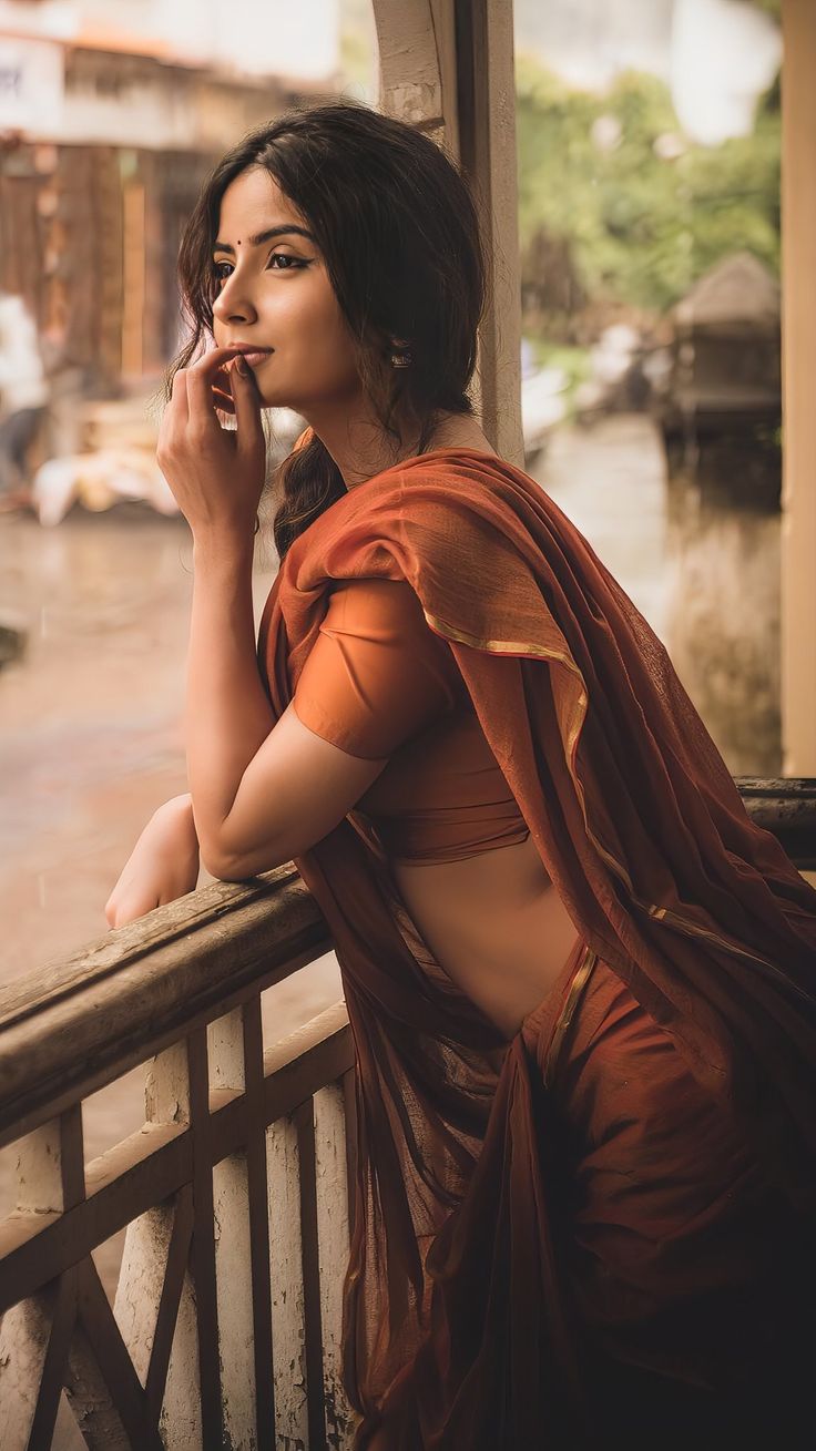 Veranda Sari Portrait with rust-orange sari, rustic railing, warm rural light, and cinematic realistic portrait mood.