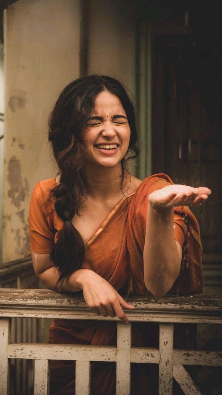 Monsoon Sari Portrait with rust-orange sari, joyful rain pose, rustic veranda railing, and warm cinematic photography mood.
